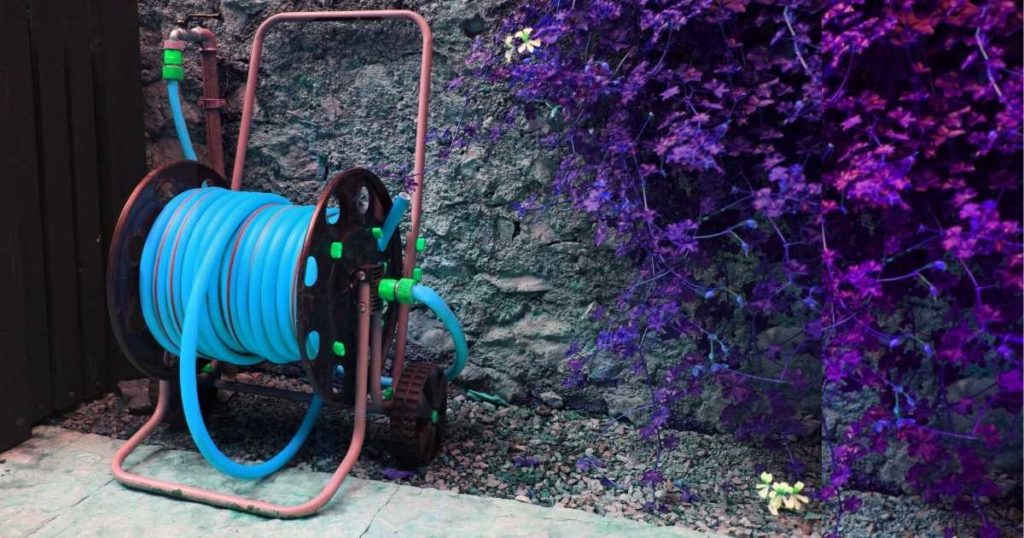 Hose reel cart with wheels with blue hose coiled near a brick wall
