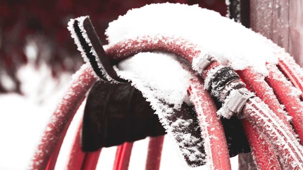 Red Garden Water Hose covered with snow in the winter freezing temperatures