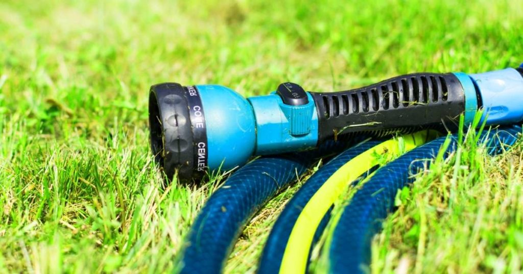 Blue hose nozzle covered with dirt on the lawn